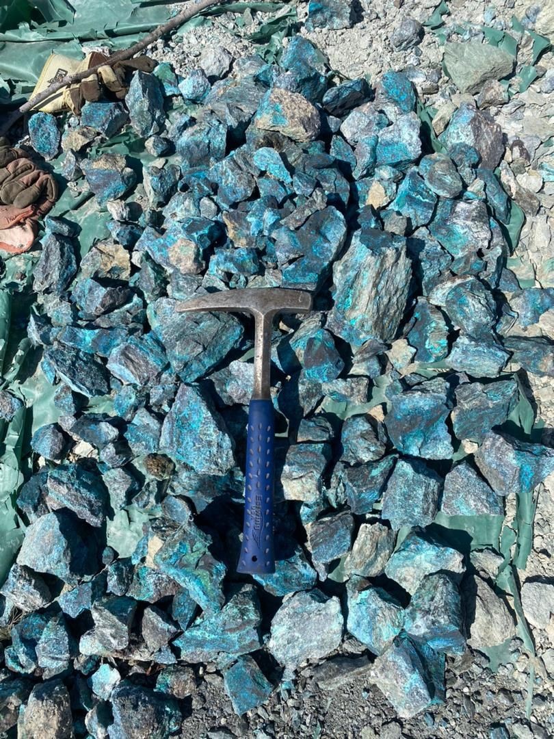 Pile of blue and grey rocks with a rock hammer and gloves placed on top.